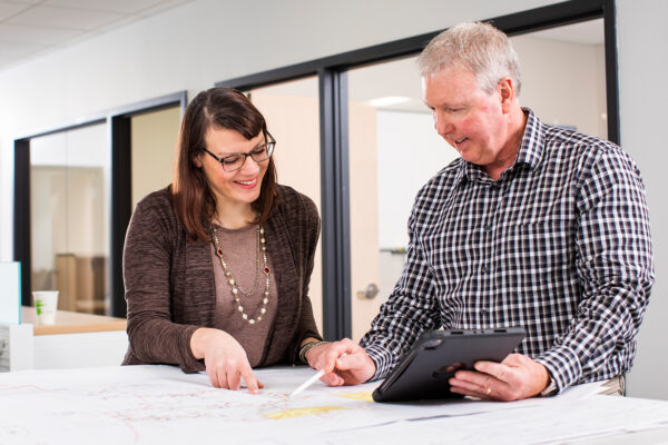 Two professionals working in an office on a design project using a tablet.