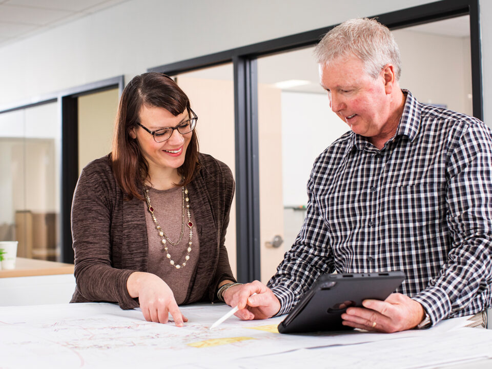 Two professionals working in an office on a design project using a tablet.