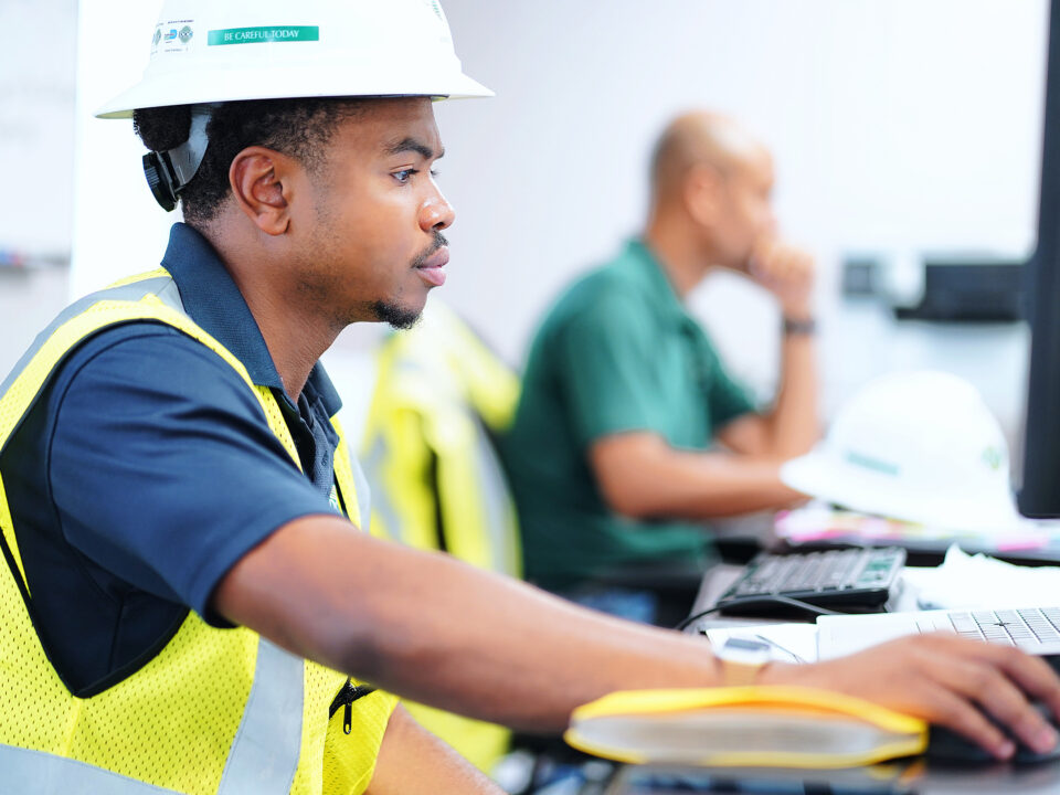 A hard hat-wearing professional engaged in computer-based tasks.