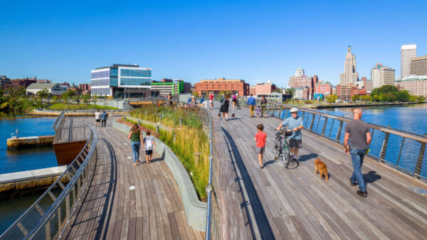 A group of people strolling on a boardwalk near a city's athletic facilities.
