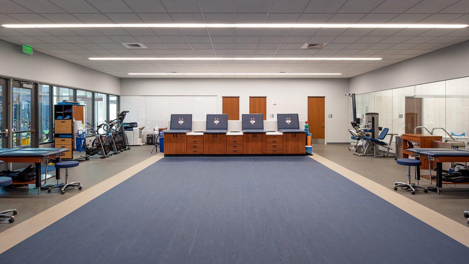 A room in the Husky Athletic Village and Rizza Performance Center with a blue floor and a lot of equipment.