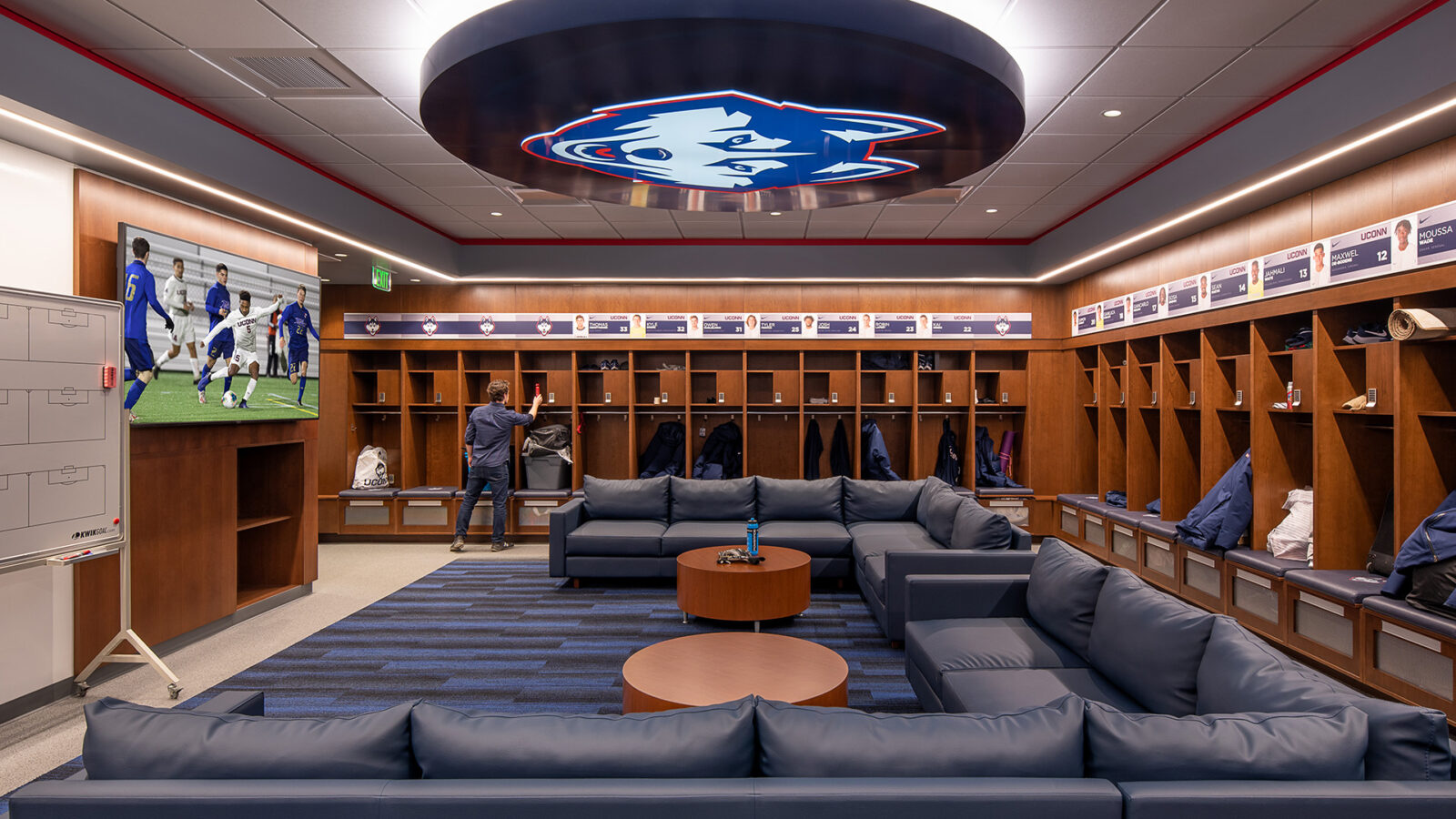 A locker room with couches and a TV located in the Husky Athletic Village and Rizza Performance Center.