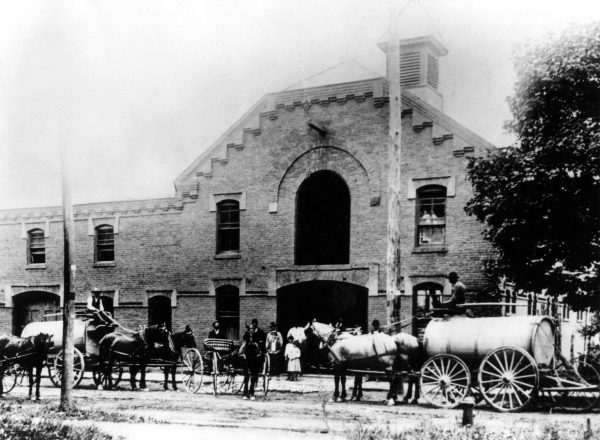 A black and white photo capturing our historical heritage with horses and wagons in front of a building.