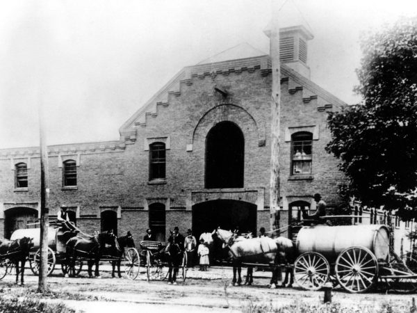 A black and white photo capturing our historical heritage with horses and wagons in front of a building.
